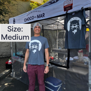 A person standing with a shirt that has Cleo Otter the mascot of Choco Del Mar on it. Size: Medium