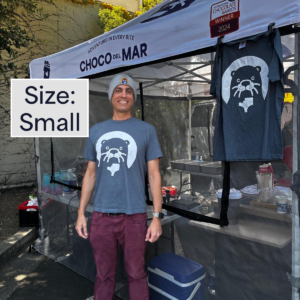A person standing with a shirt that has Cleo Otter the mascot of Choco Del Mar on it. Size: Small