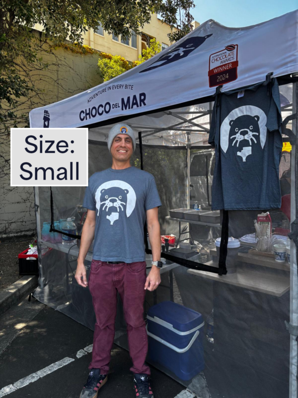A person standing with a shirt that has Cleo Otter the mascot of Choco Del Mar on it. Size: Small
