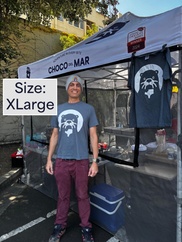 A person standing with a shirt that has Cleo Otter the mascot of Choco Del Mar on it. Size: Extra Large
